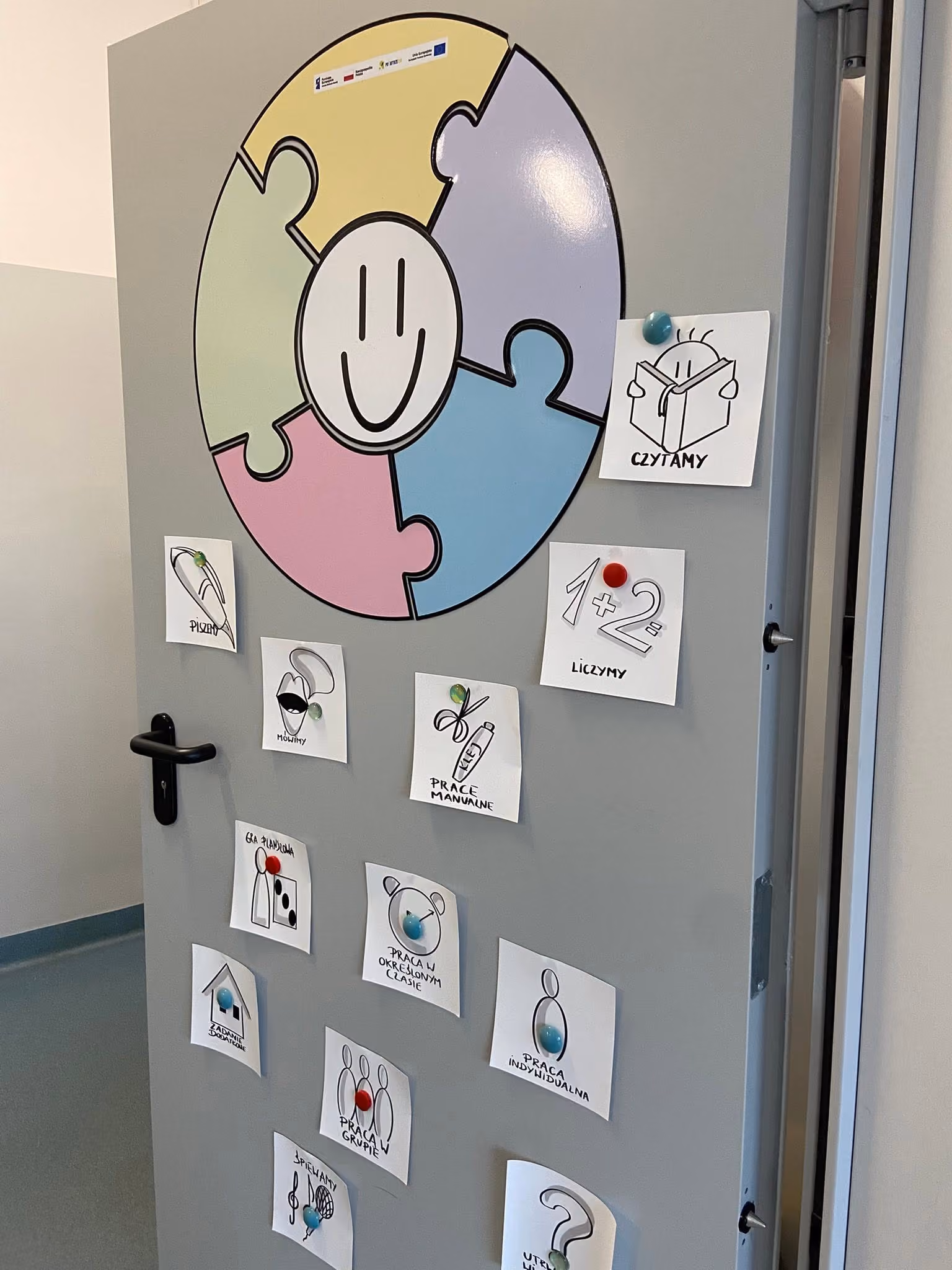 Drzwi sali z puzzlą afazJA – możeMY i karteczkami ikon ToDoList: czytamy, liczymy, prace manualne, praca w grupie.